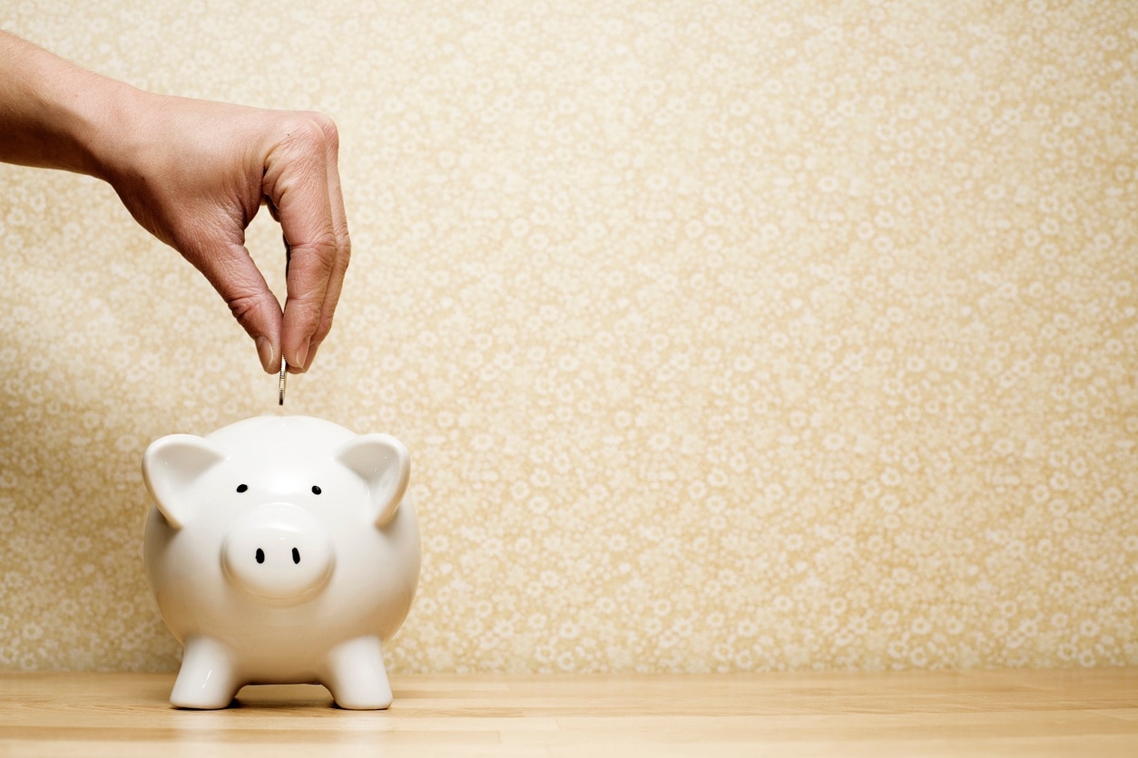 a person's hand deposits a coin into a piggy bank