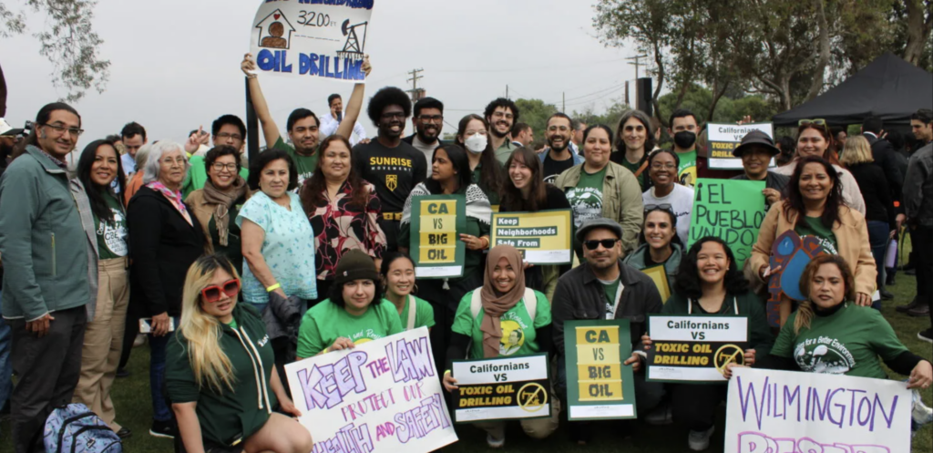 A group of determined people holding signs in Spanish and English, protesting against toxic oil drilling in their community.